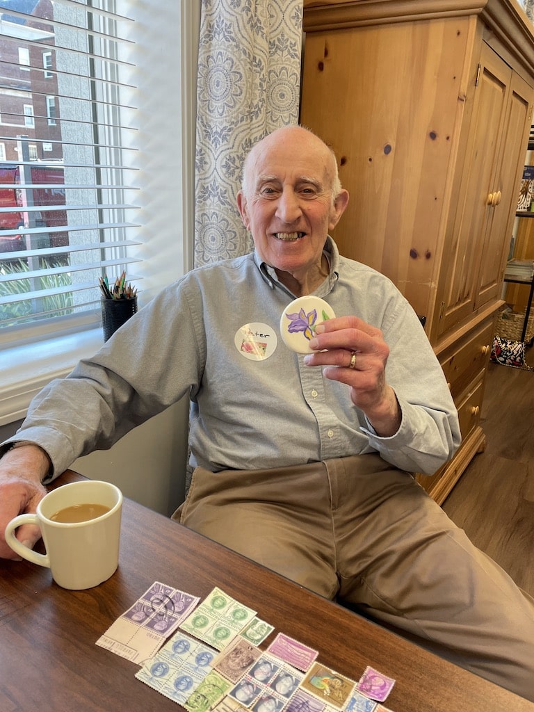 An elderly man smiling and holding up a stamp-inspired button